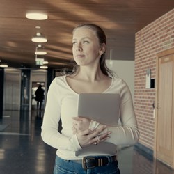Female student walking through the hallways at NHH campus carrying a  laptop in her arms